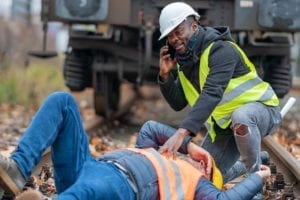 Railroad employee calling for help on a cell phone for an injured railroad employee laying on the tracks.